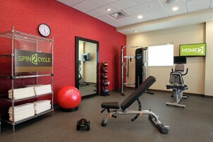Un gimnasio con equipo de ejercicio, una pared roja, un reloj y un letrero que dice 'HOME 2'.