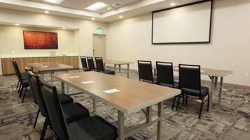 A conference room with a long table, multiple chairs, a projector screen, and a carpeted floor.