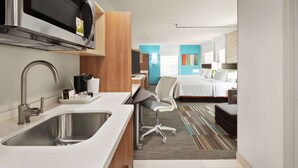 A compact hotel room with a kitchenette, a bed, a desk, and a chair. - Home2 Suites by Hilton Woodbridge Potomac Mills (Woodbridge)