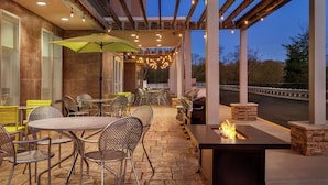 An outdoor patio area with tables and chairs, a fire feature, and string lights. - Home2 Suites by Hilton Woodbridge Potomac Mills (Woodbridge)