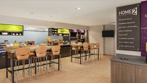 A modern kitchen with bar seating, a coffee station, and a sign for "inspirited table". - Home2 Suites by Hilton Woodbridge Potomac Mills (Woodbridge)