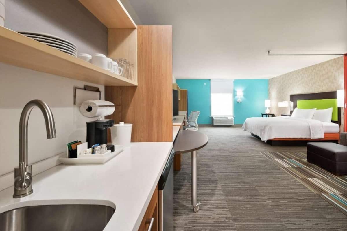 Ein Hotelzimmer mit einer Küchenzeile, einem Bett, einem Schreibtisch und einem Stuhl.