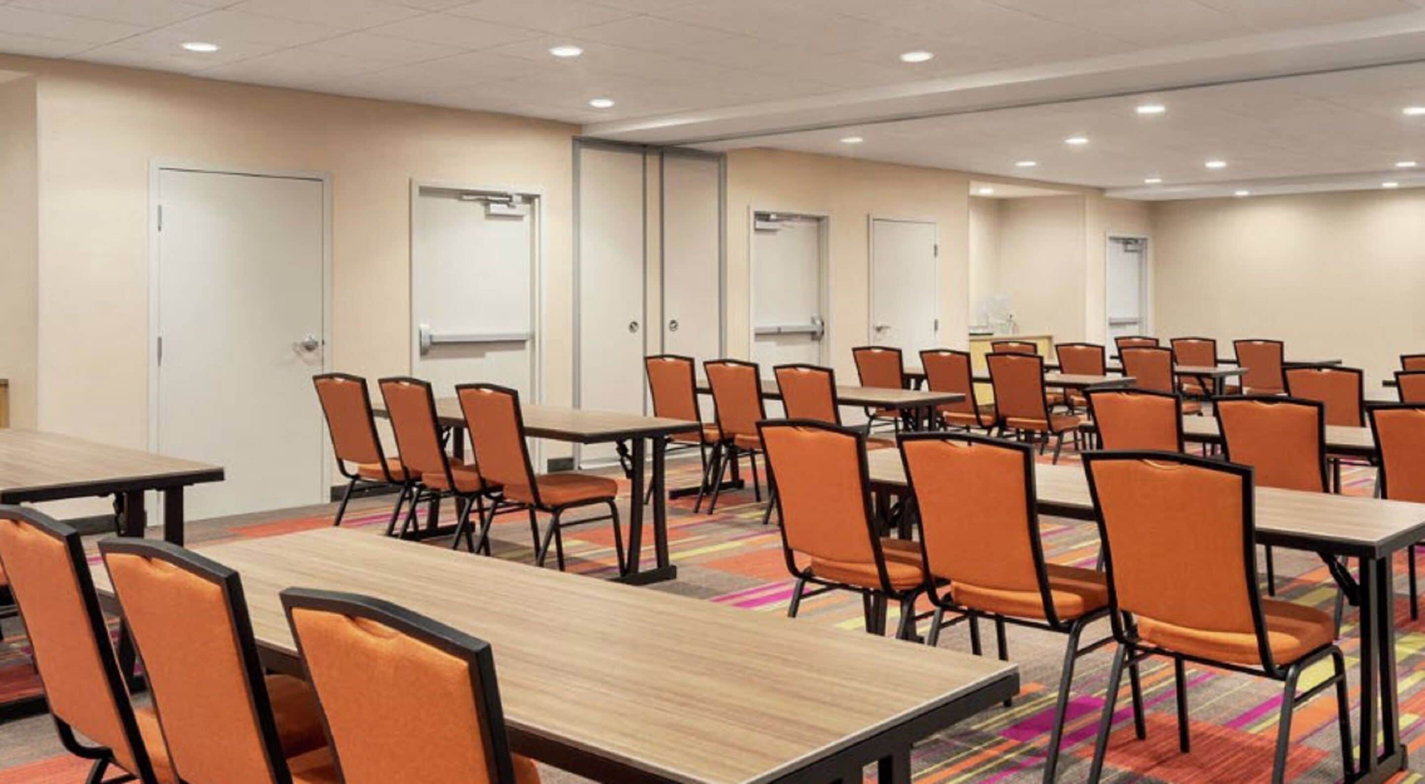 Una sala conferenze con vari tavoli e sedie, pareti bianche e pavimento rivestito di moquette.