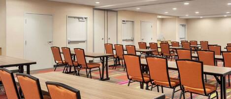 A conference room with multiple tables and chairs, white walls, and a carpeted floor.