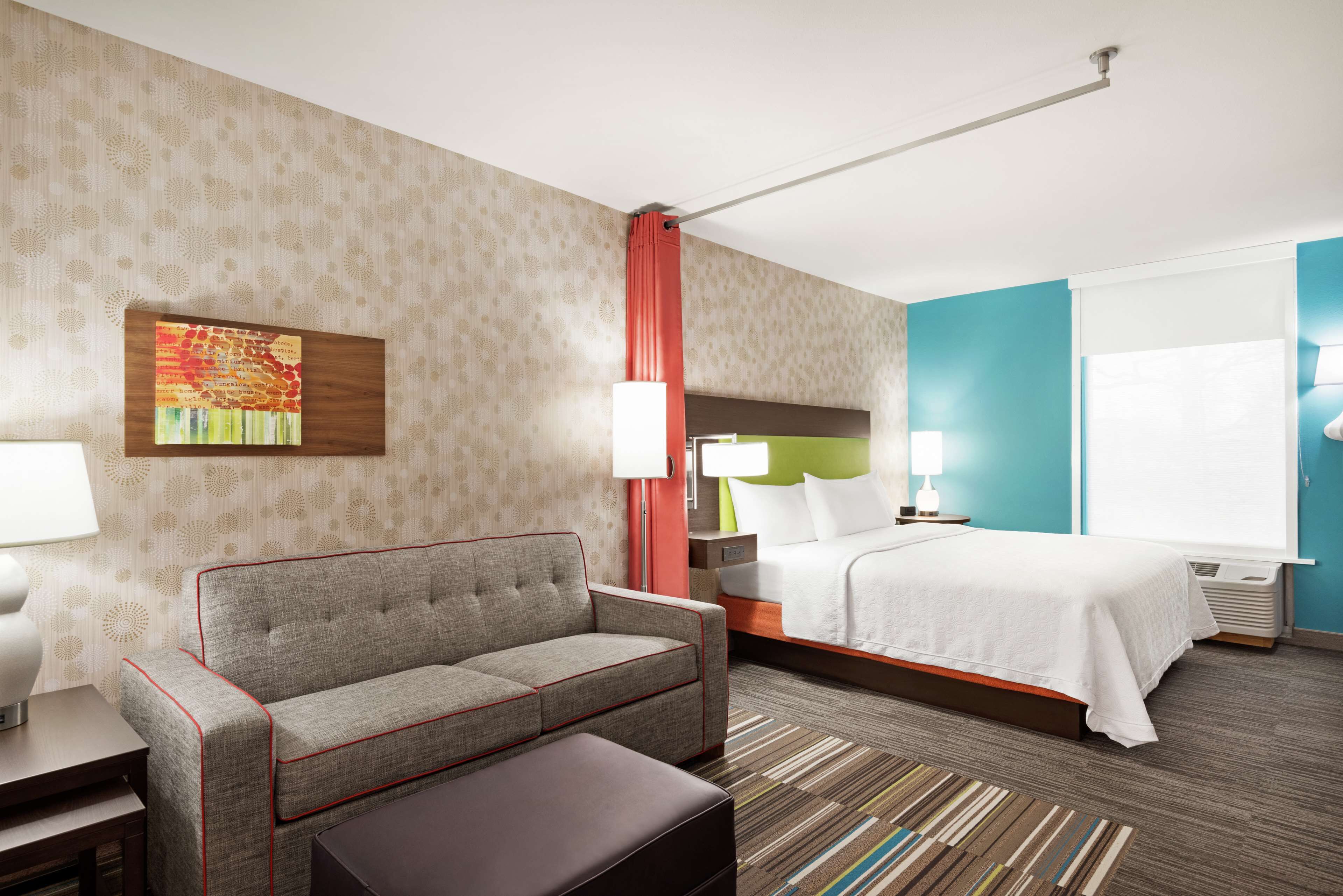 Une chambre d’hôtel avec un canapé, un lit, une table de chevet, une lampe et un tableau au mur.