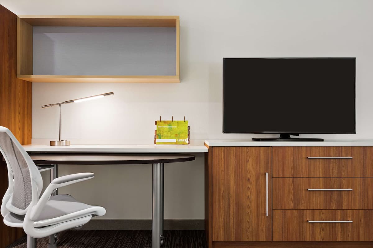 Ein moderner Arbeitsraum mit Schreibtisch, Stuhl, Lampe, Bücherregal und einem Fernseher.
