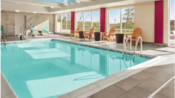 An indoor swimming pool with a clear view of the sky through large windows, a pool ladder, and several lounge chairs. - Home2 Suites by Hilton Woodbridge Potomac Mills (Woodbridge)