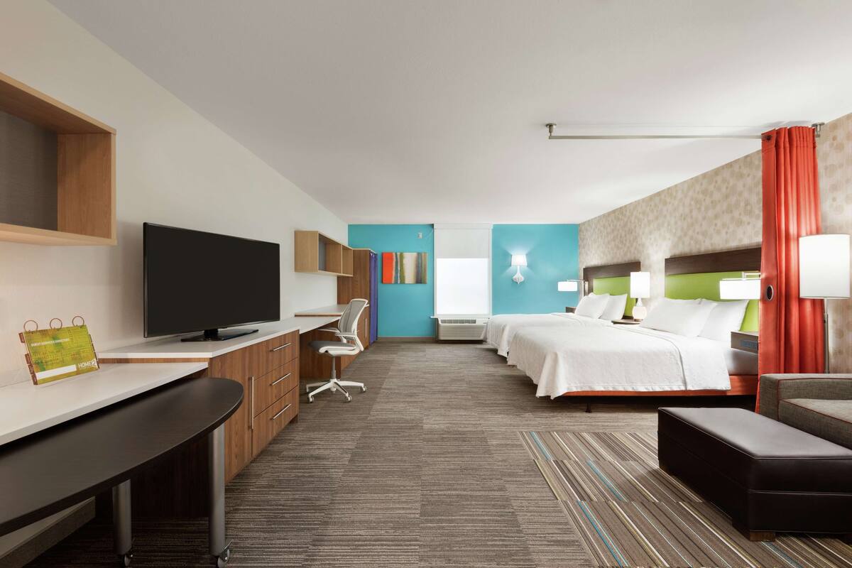 Ein Hotelzimmer mit Schreibtisch, Fernseher, zwei Betten und einem großen Fenster.