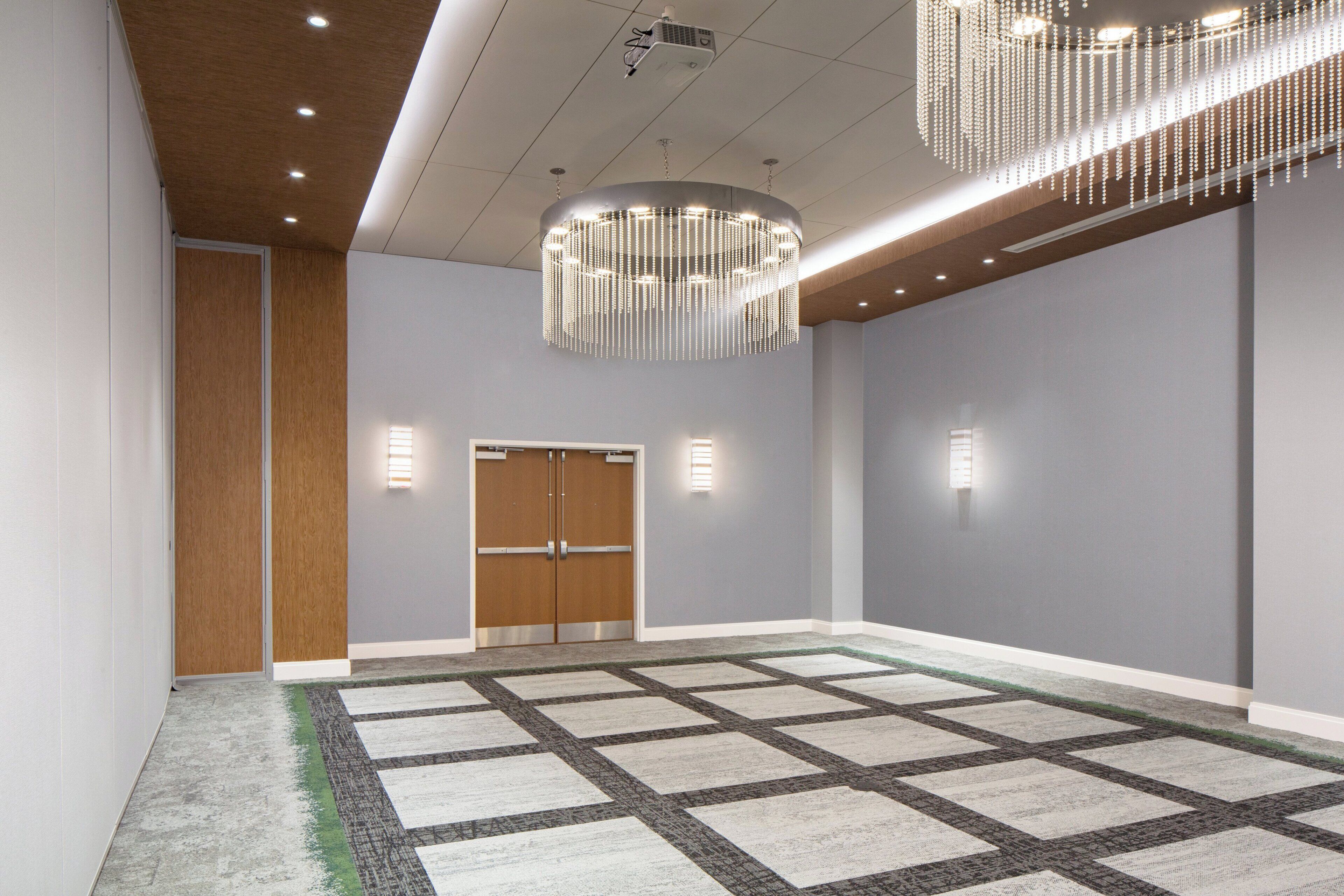 A spacious room with a large carpeted area, a wooden door, and a modern chandelier.