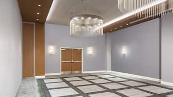 A spacious room with a large carpeted area, a wooden door, and a modern chandelier.