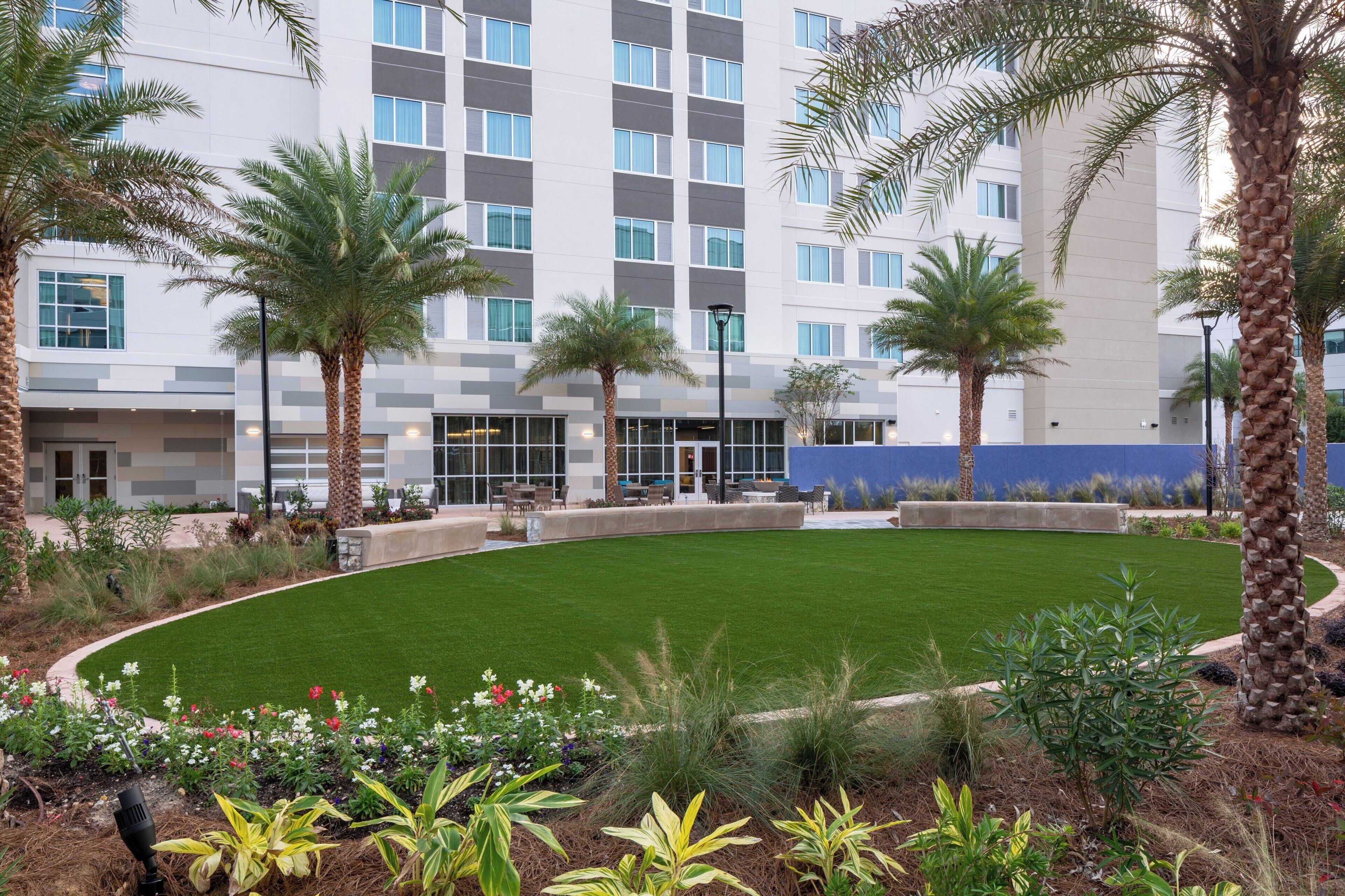 A landscaped courtyard with palm trees, a well-maintained lawn, and a building with multiple windows and balconies.