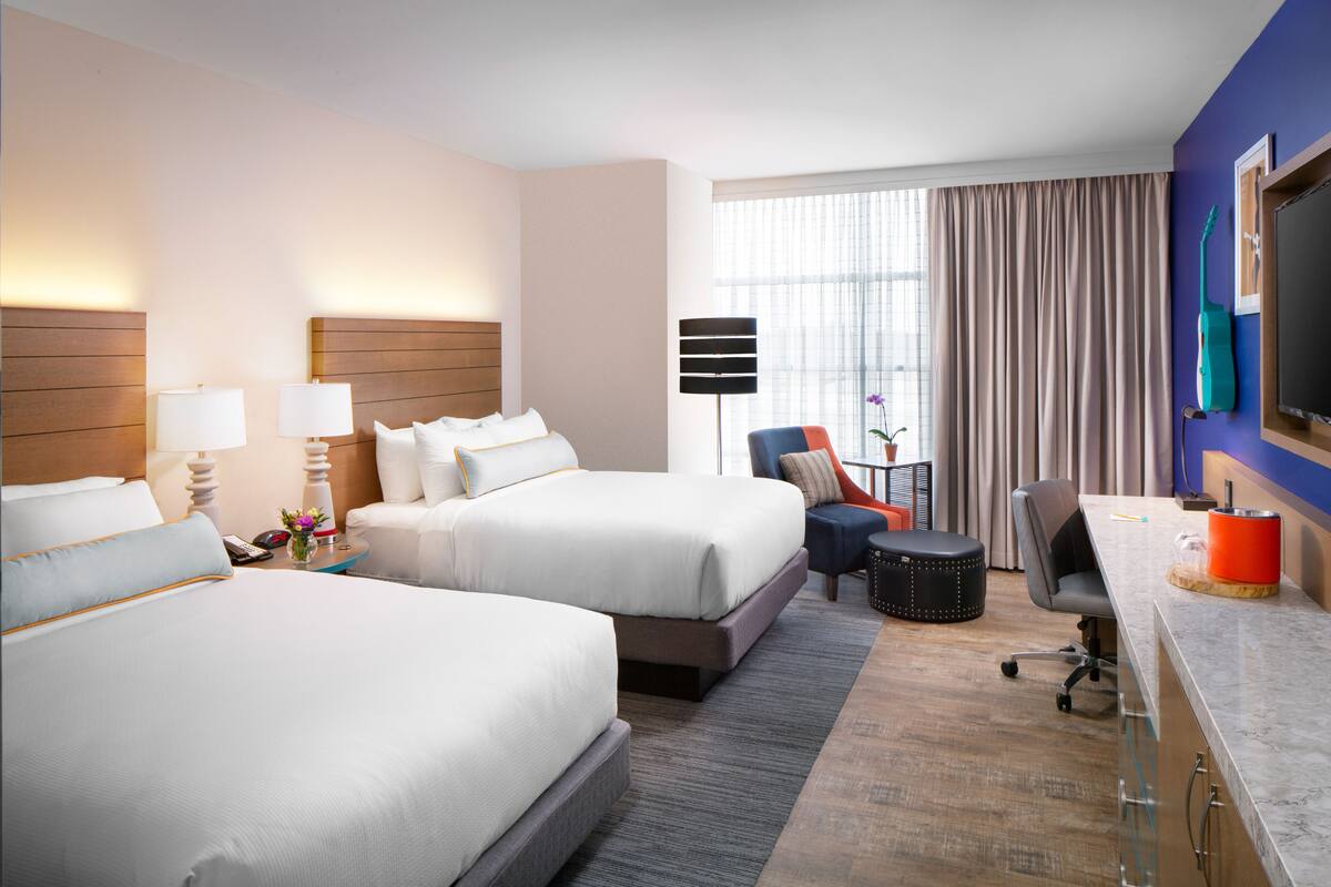 Une chambre d’hôtel avec deux lits, un bureau, une chaise, une télévision et une fenêtre avec des rideaux.