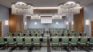 A conference room with rows of green chairs, a large screen, and two chandeliers.