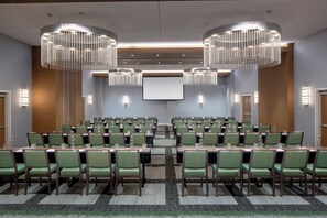 A conference room with rows of green chairs, a large screen, and two chandeliers. - Hotel Indigo Gainesville-Celebration Pointe by IHG (Gainesville)