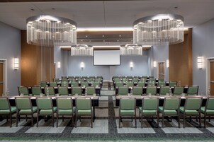 Un salón de conferencias con hileras de sillas verdes, una pantalla grande y dos candelabros.
