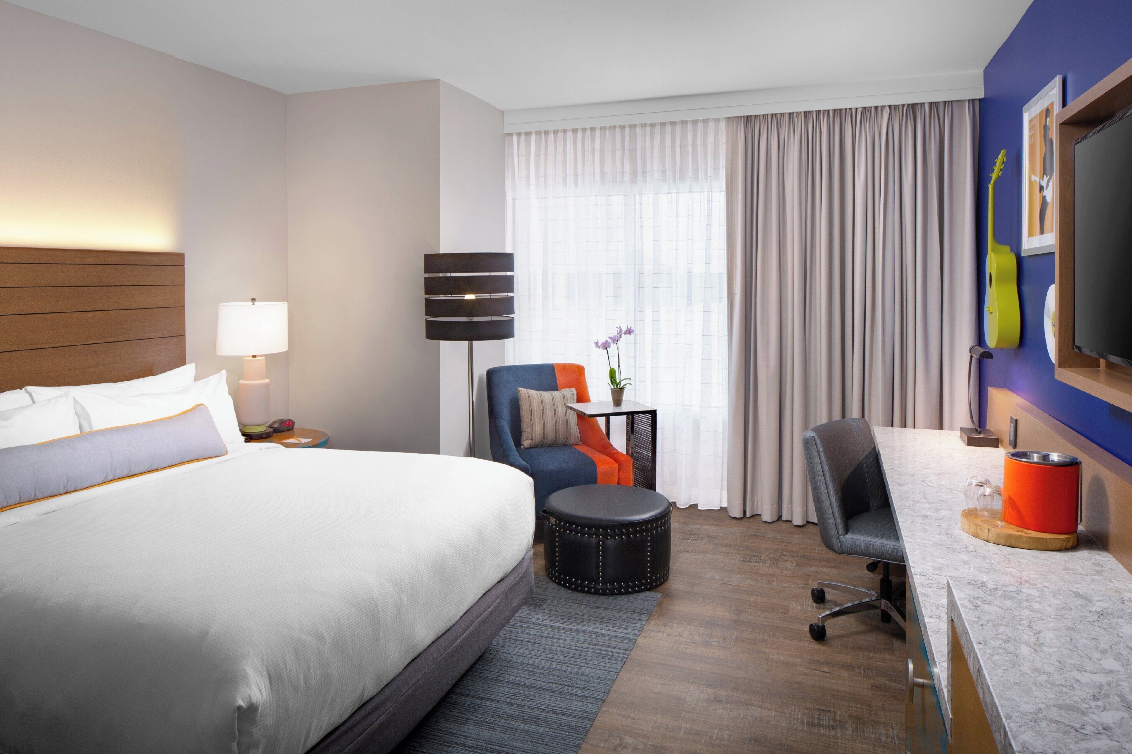 Une chambre d’hôtel avec un grand lit, un bureau, une chaise, une lampe et un téléviseur.