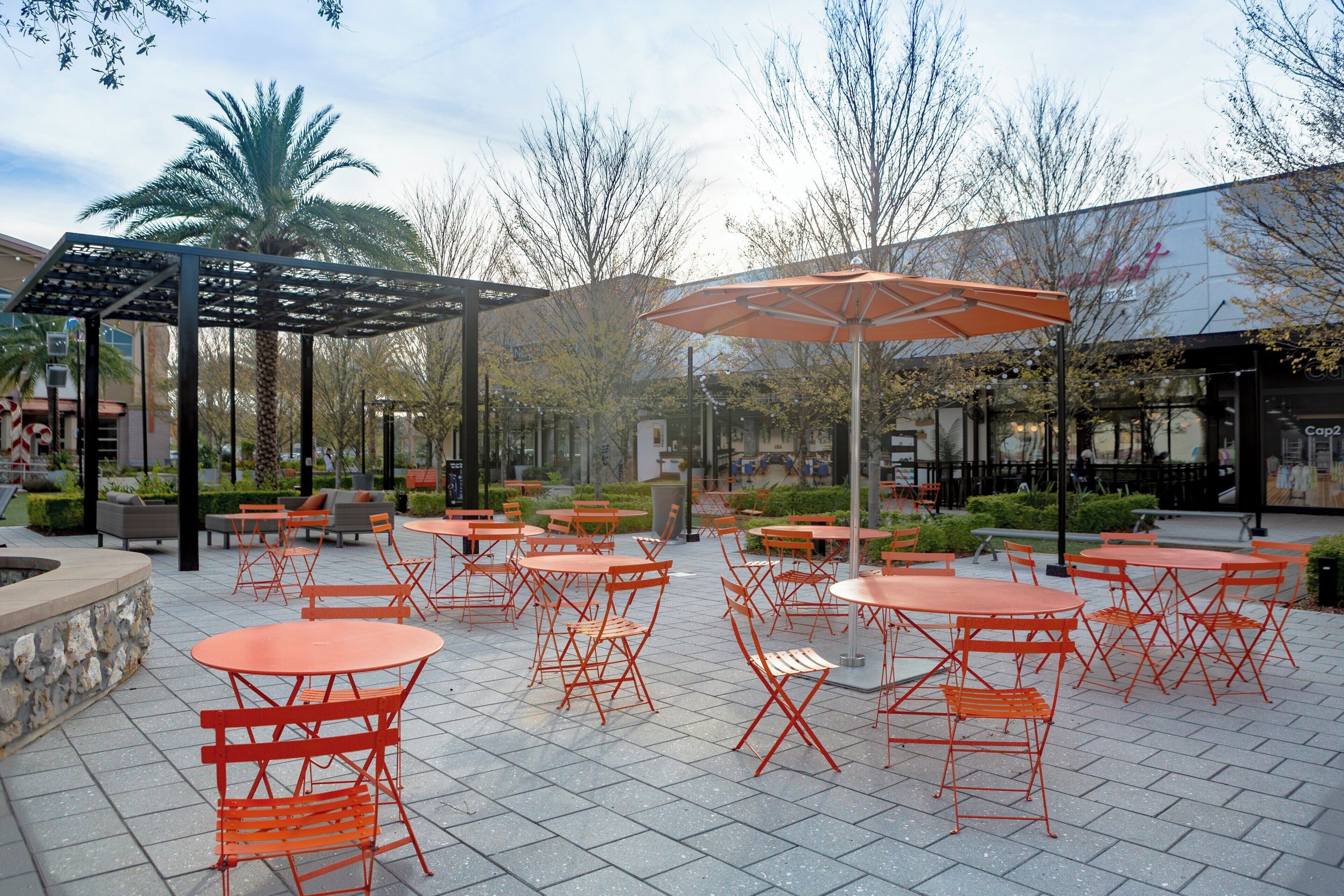 Un patio al aire libre con mesas y sillas anaranjadas, una zona de estar cubierta y un edificio en el fondo.