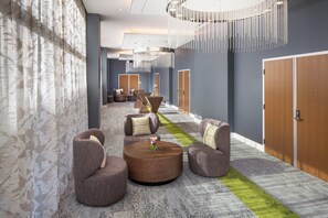 A modern hotel lobby with a long reception desk, seating area, and a decorative chandelier. - Hotel Indigo Gainesville-Celebration Pointe by IHG (Gainesville)