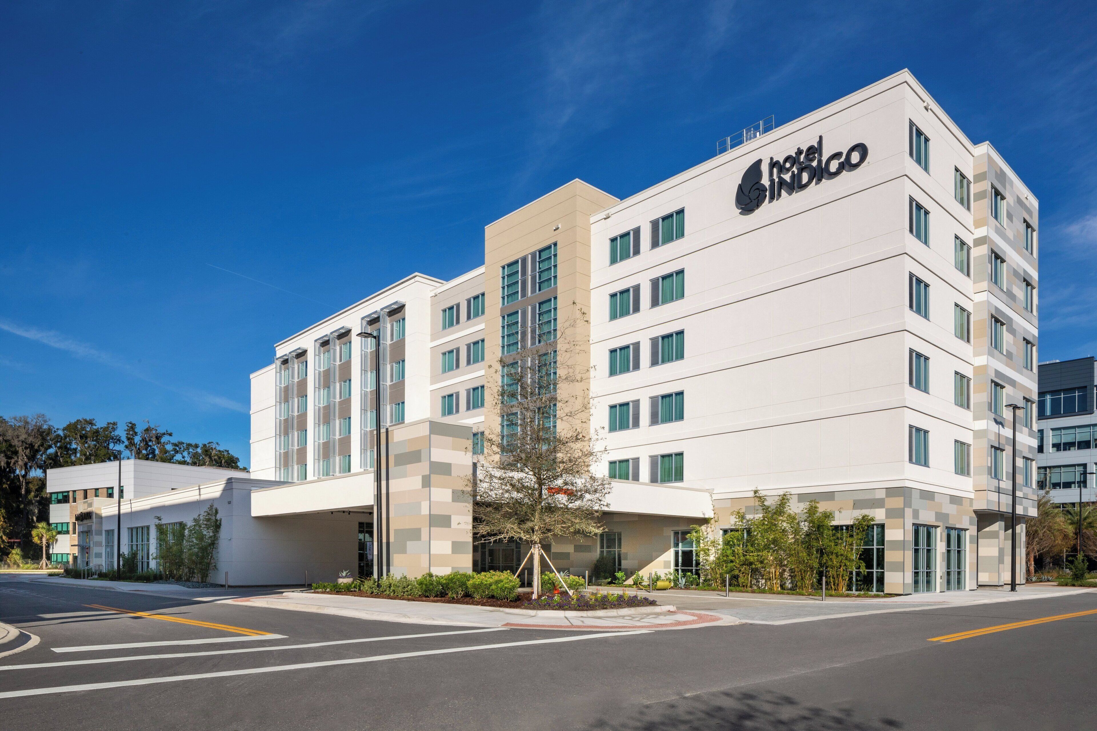 A modern hotel building with a prominent logo, multiple floors, and a parking area in front.