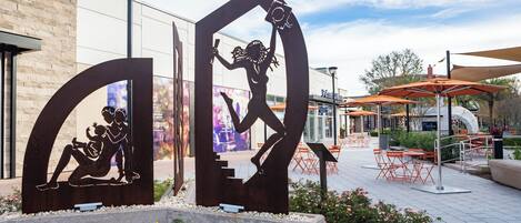 Outdoor seating with tables and chairs, a decorative metal sculpture, and a building with signage.