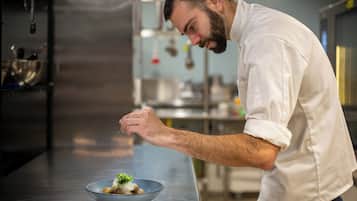 A chef in a white shirt preparing food in a kitchen with stainless steel appliances and a metal bowl on the counter.