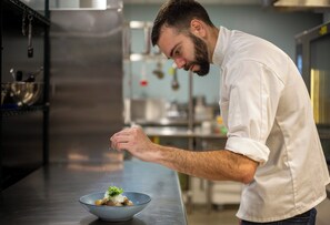 A chef in a white shirt preparing food in a kitchen with stainless steel appliances and a metal bowl on the counter. - Hotel Indigo Gainesville-Celebration Pointe by IHG (Gainesville)