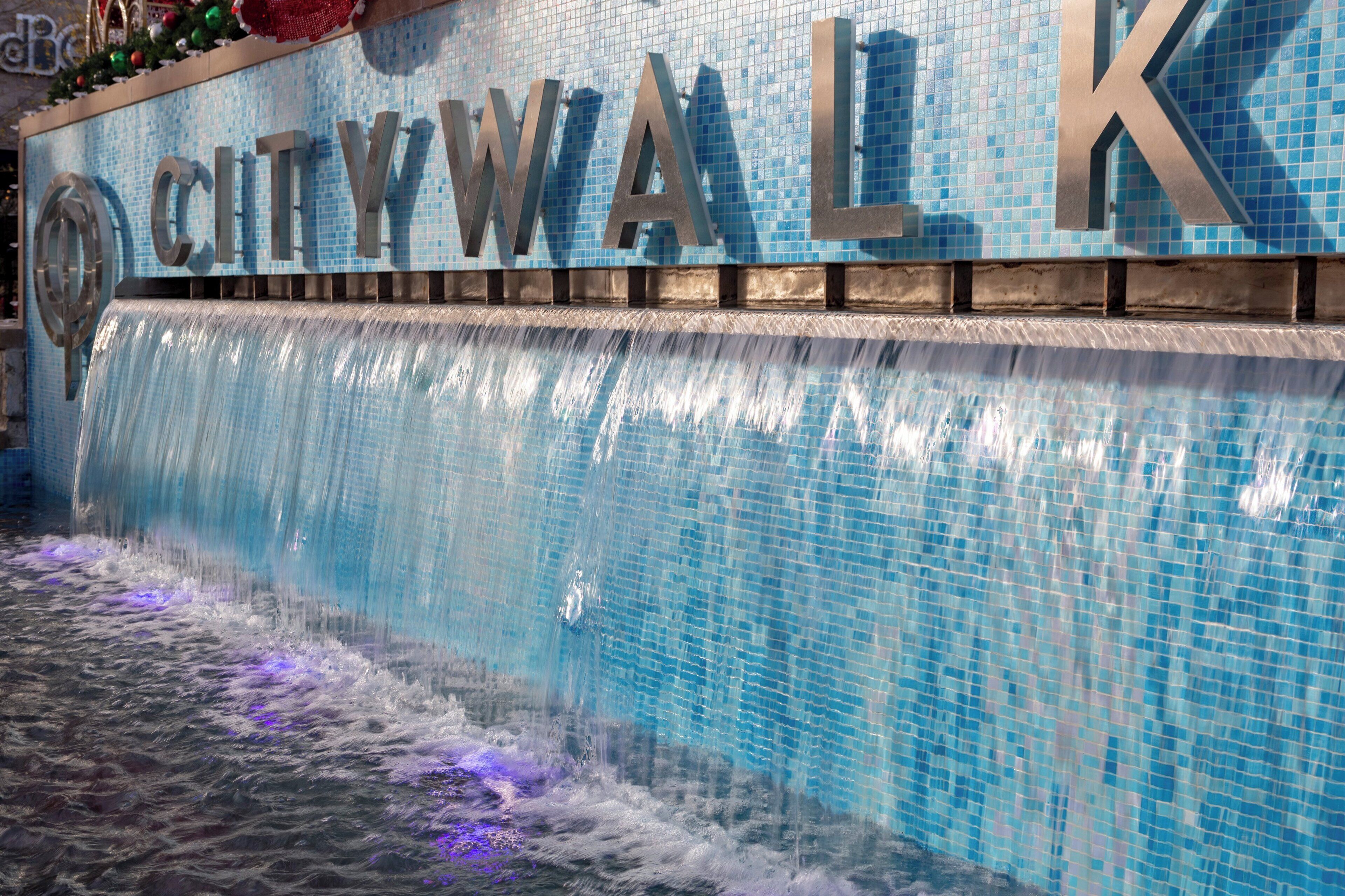 Una fuente con las palabras 'CITYWALK' en letras grandes, un muro con azulejos y una cascada.