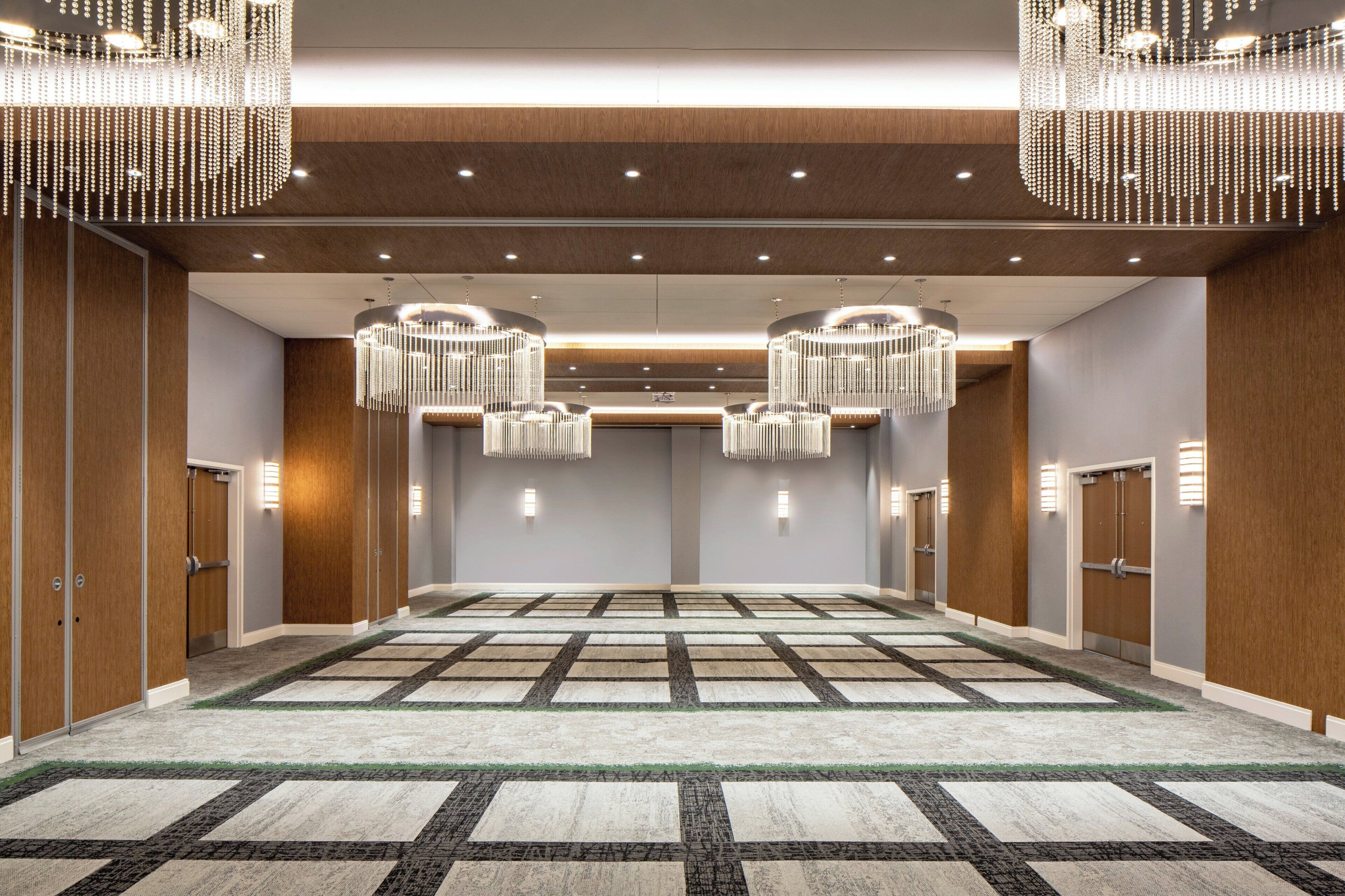 Un amplio vestíbulo de hotel con alfombra a cuadros, paneles de madera y dos grandes candelabros.