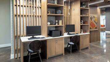 Un espacio de oficina moderno con dos escritorios, cada uno con monitor, teclado y ratón. Hay dos sillas, una pared decorativa con estanterías y un suelo estampado.