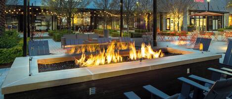 Een terras met een vuurplaats, stoelen en tafels.
