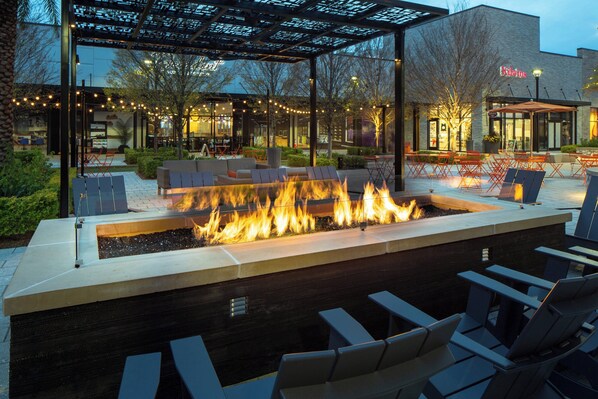An outdoor seating area with a fire feature, chairs, and tables.