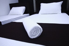 A neatly made bed with a rolled white towel on a black bedspread, a white pillow, and a headboard. - Yoho Bro Colombo 03 (Colombo)
