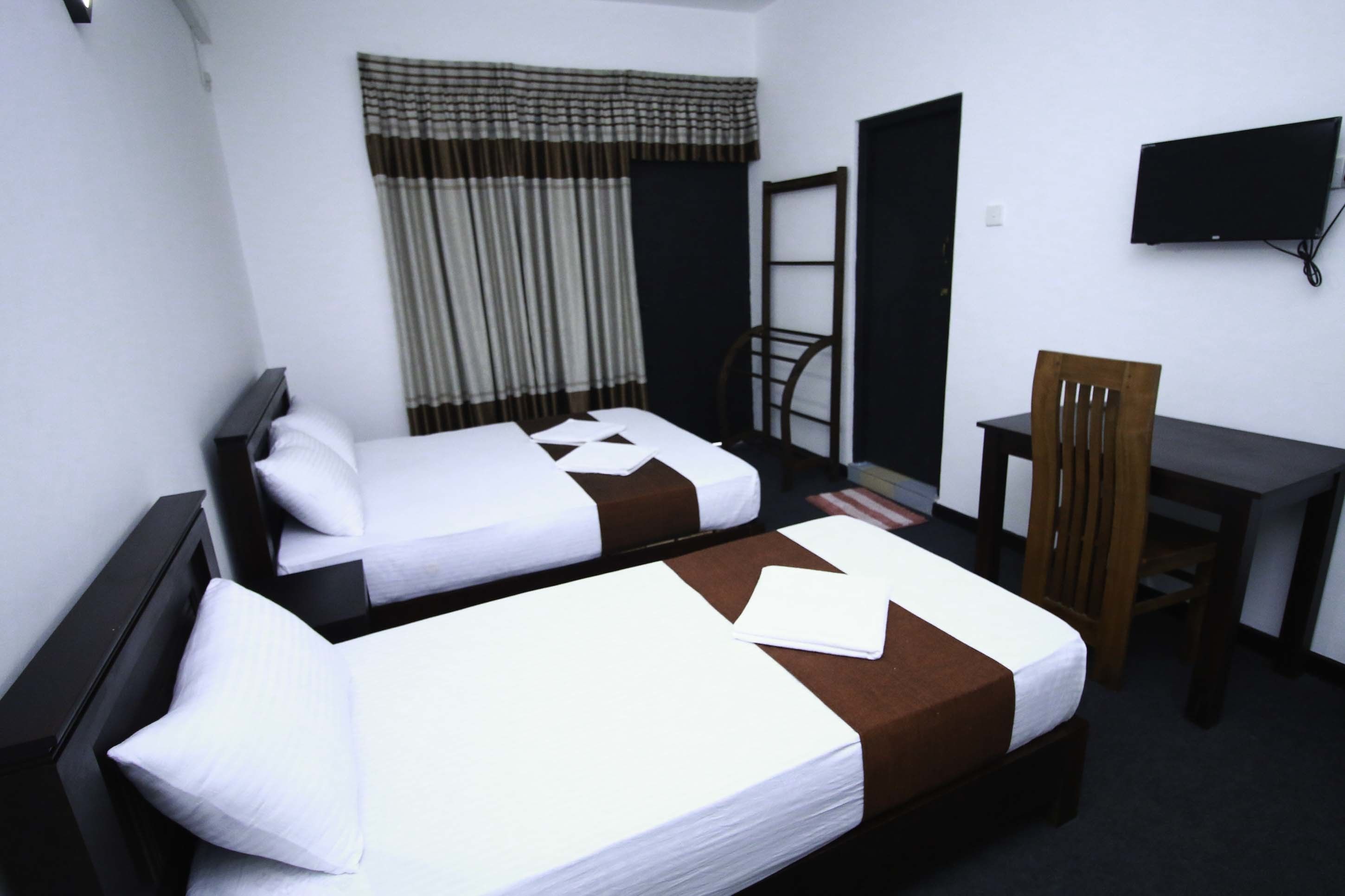 A hotel room with two beds, a desk, a chair, a television, and a window with curtains.