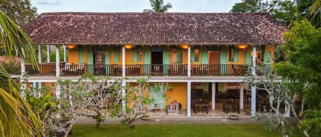 A two-story building with a tiled roof, green shutters, and a balcony with wooden railings.