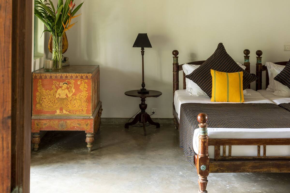 A bedroom with a bed, a ceiling fan, a bedside table, a lamp, and a decorative box with a plant.