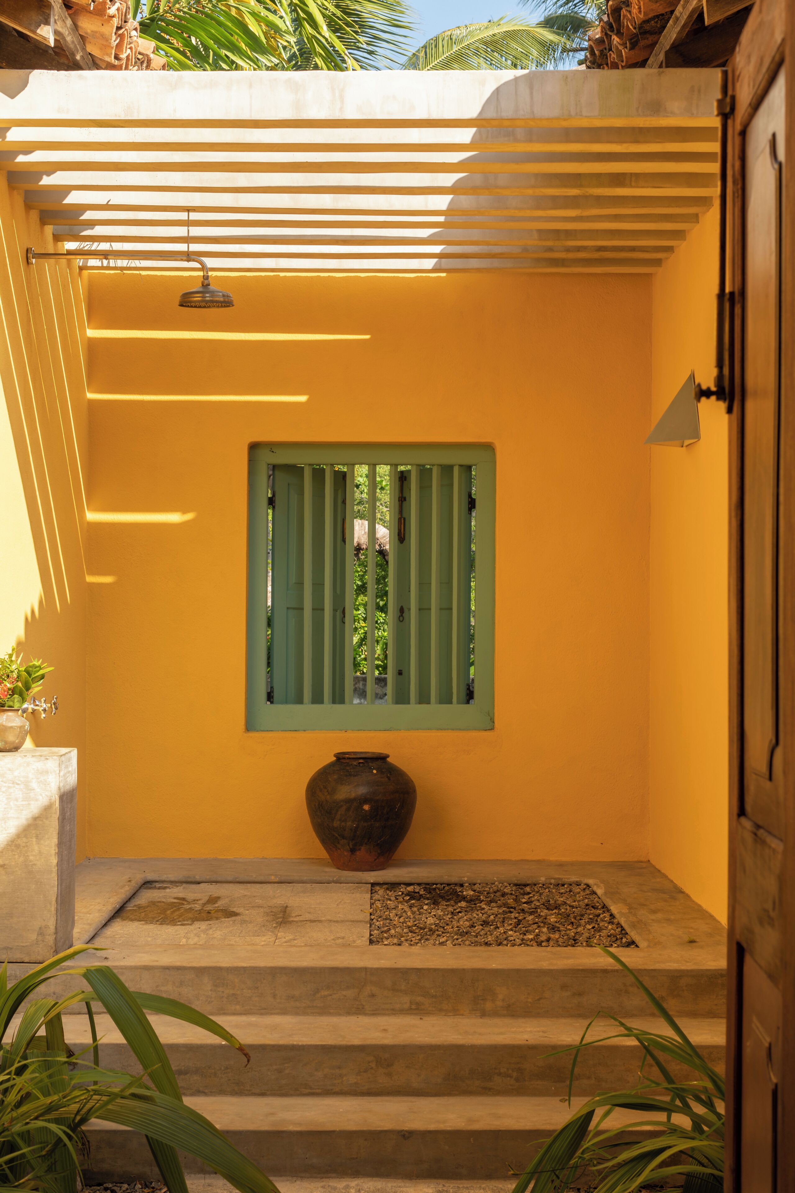 A staircase leading to a door with a green window, a large vase, and a small plant on the steps.