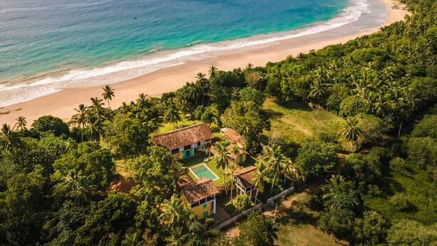 An aerial view of a beach resort with a clear view of the ocean, sandy beach, and lush greenery. - The Last House (Morakatiyara)