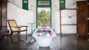 A bathroom with a freestanding bathtub, a wooden chair, a small table, and a door with a decorative panel. - The Last House (Morakatiyara)