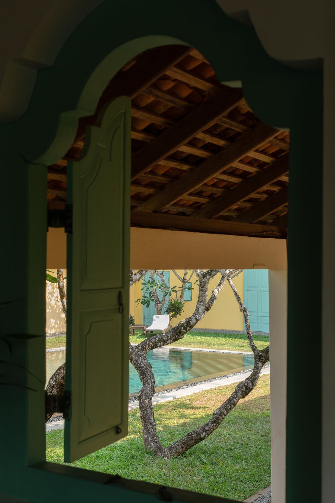 Puerta abierta que da a una zona de piscina, con vista a un árbol y un edificio al fondo.