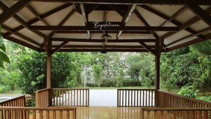 Un espace extérieur abrité, doté d’un banc en bois et d’un sol carrelé, et entouré de verdure.