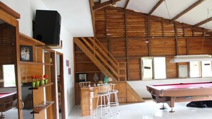 Une pièce spacieuse équipée d’une table de billard, d’un coin bar et d’un escalier menant à un niveau supérieur.
