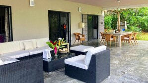 Een overdekt terras met een bank, stoelen en een tafel.