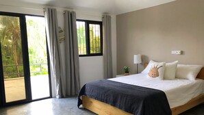 Een slaapkamer met een groot bed, een nachtkastje met een lamp en uitzicht op groen buiten het raam.