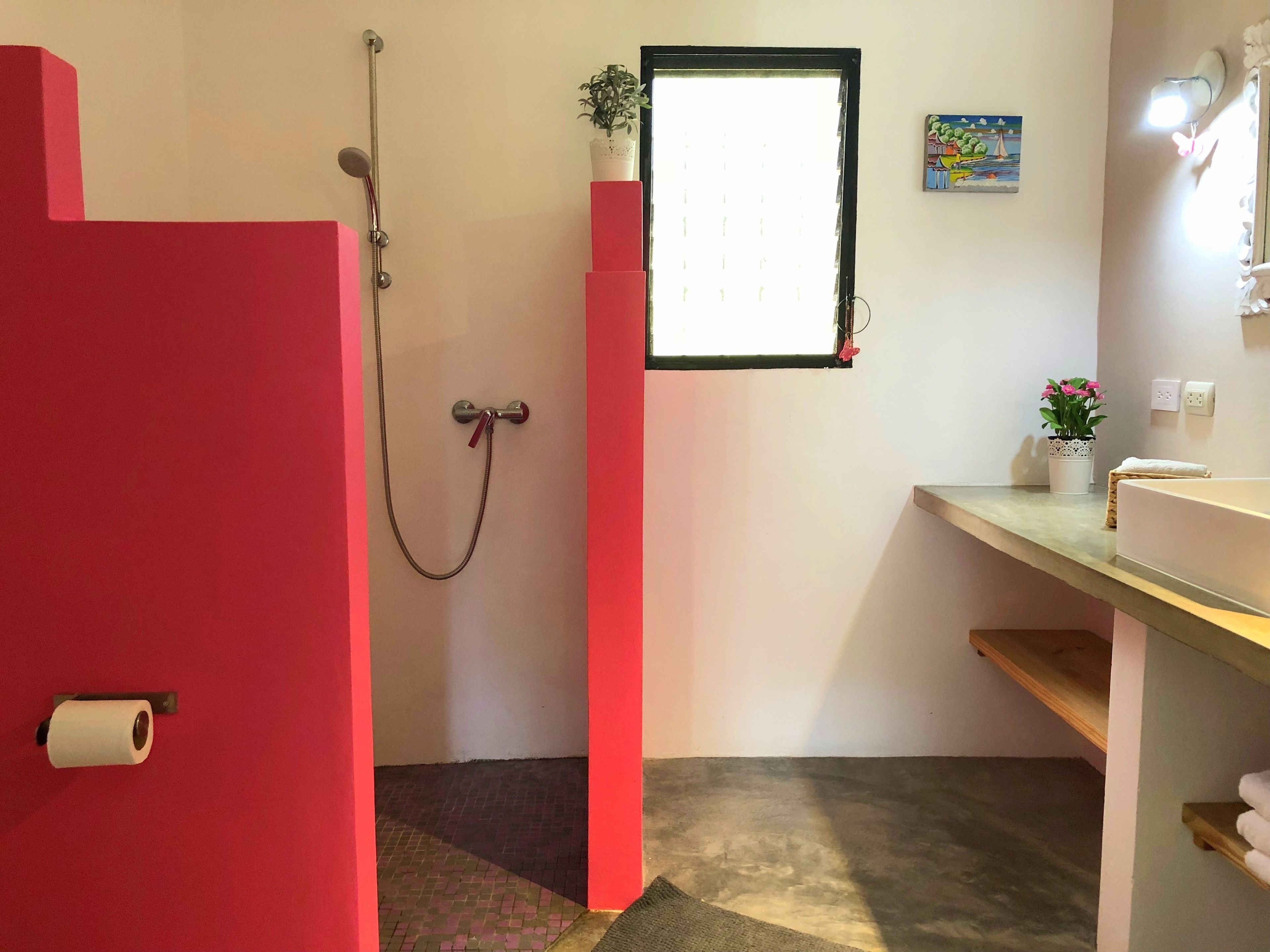 Een badkamer met een douche, een wastafel en een klein raam.