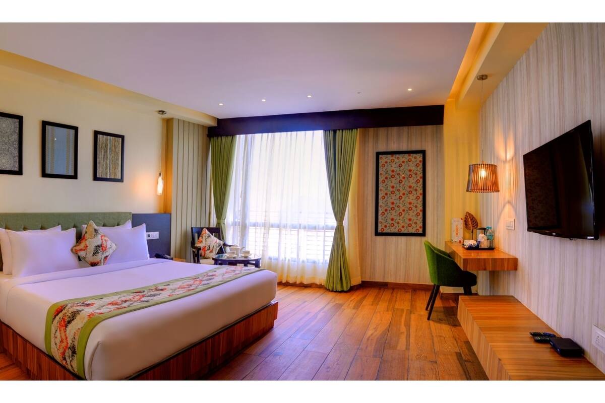 Habitación de hotel con una cama grande, un escritorio, una silla, un televisor y una ventana con cortinas.