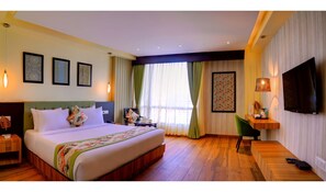 A hotel room with a large bed, a desk, a chair, a TV, and a window with curtains. - Udaan Clover Hotel Banquet & Spa (Jalpaiguri)