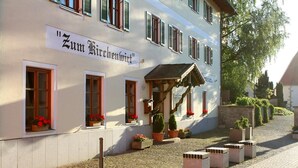 A building with a sign reading "Zum Kirchenviertel". It has multiple windows with flower boxes, a small porch with a roof, and potted plants around the entrance. - Landgasthof Zum Kirchenwirt (Thyrnau)