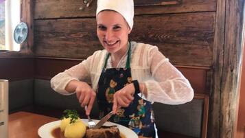 En person i hvid kokkehue og forklæde skærer kød på en tallerken med to dumplings og pynt.