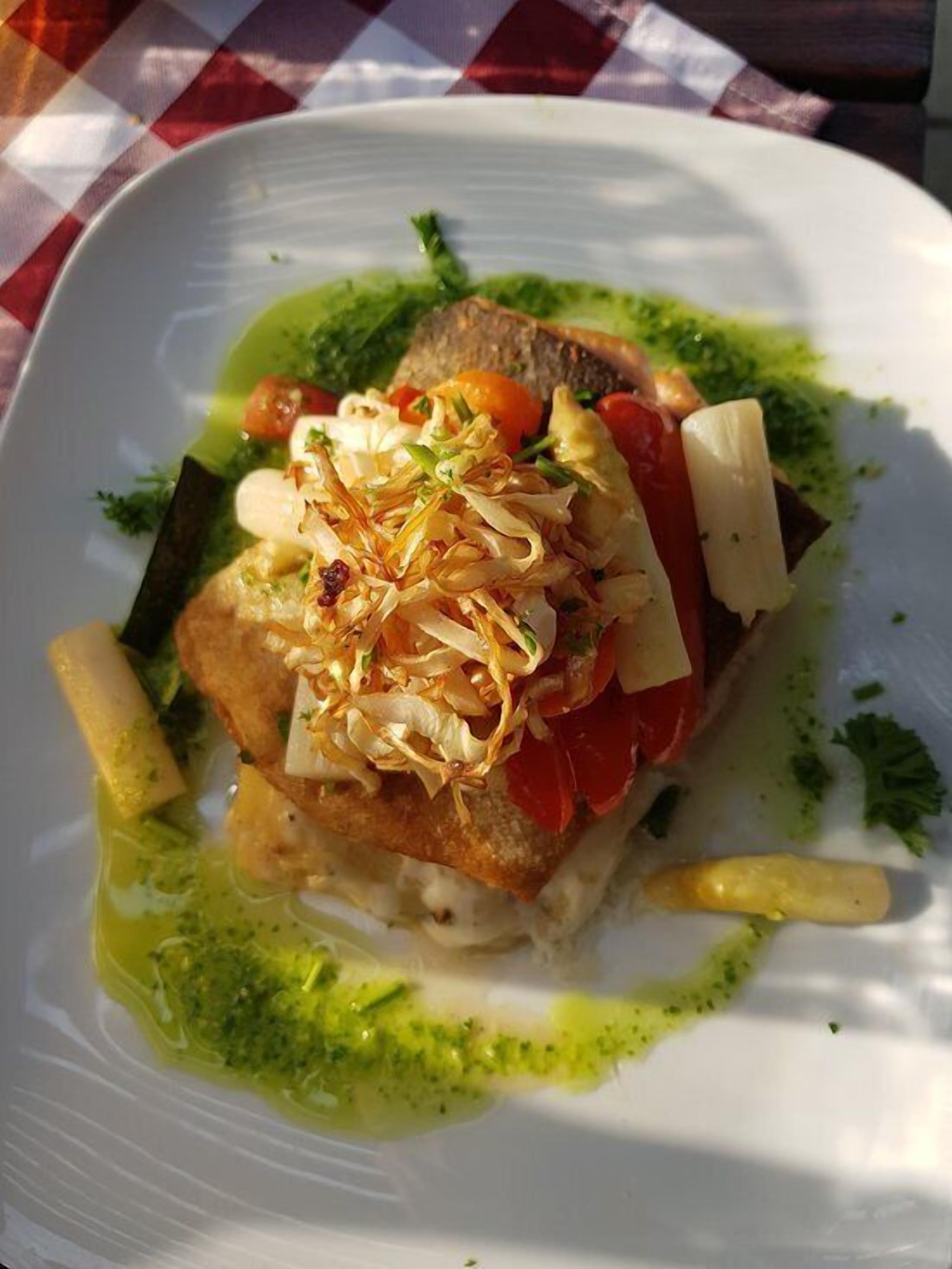 Un plato de comida con un trozo de pescado, verduras y salsa verde.