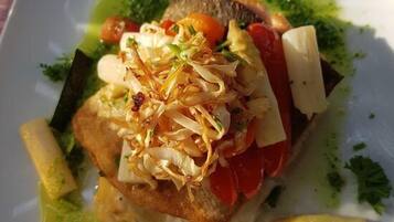 A plate of food with a piece of fish, vegetables, and a green sauce.